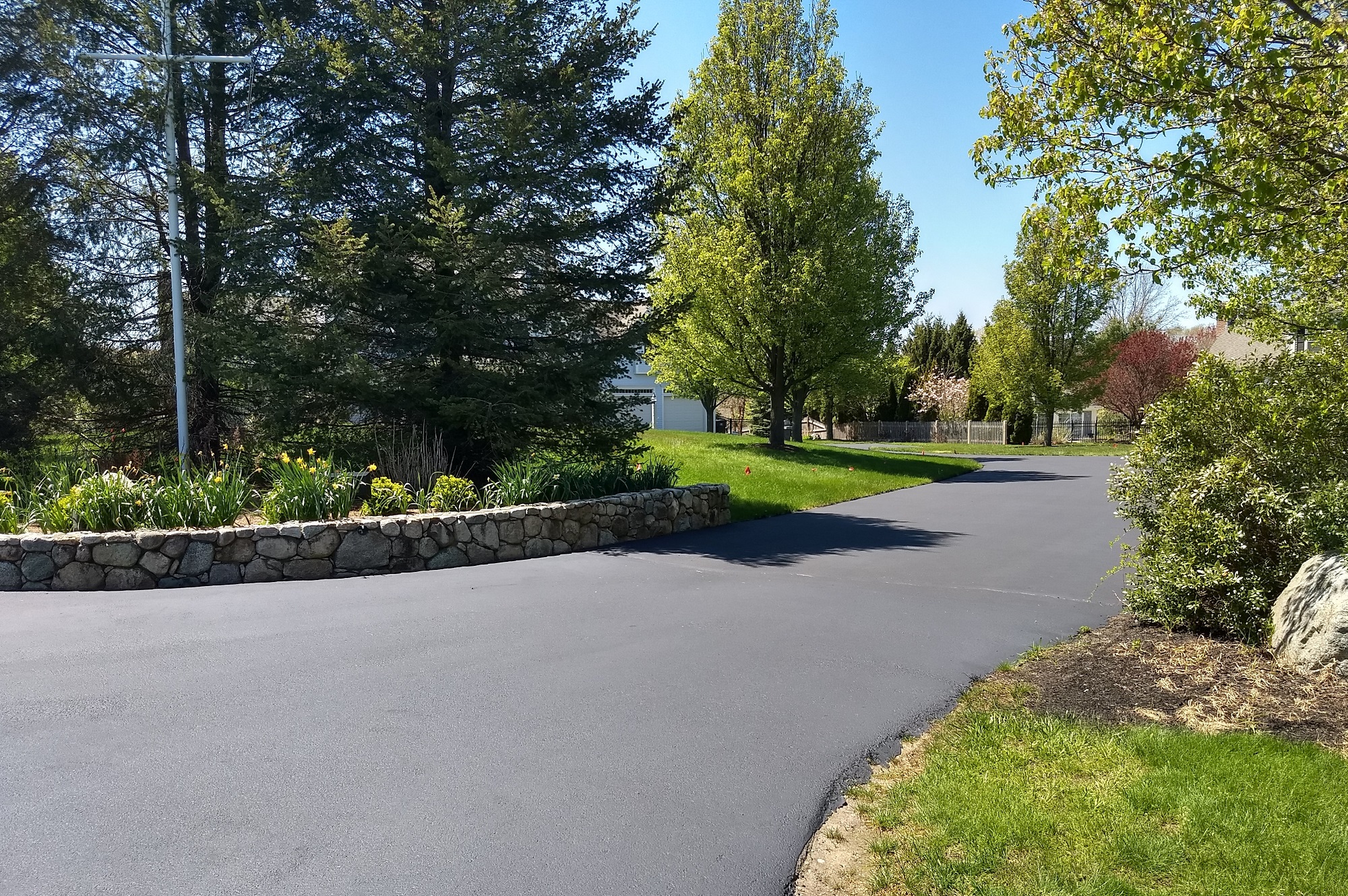 New sealcoating on a driveway with a curved stone wall with a garden. A very tranquil setting.