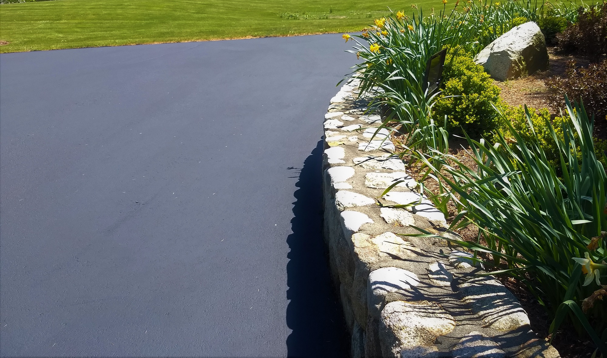 A curved stone wall and garden has an ultra neat appearance after new sealcoating.