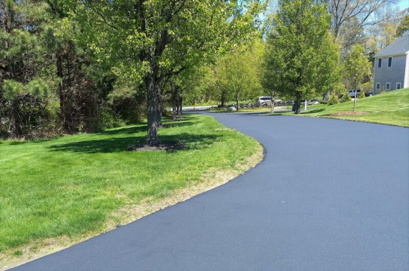 A long winding driveway lined by lawn and trees is protected by new sealcoating.